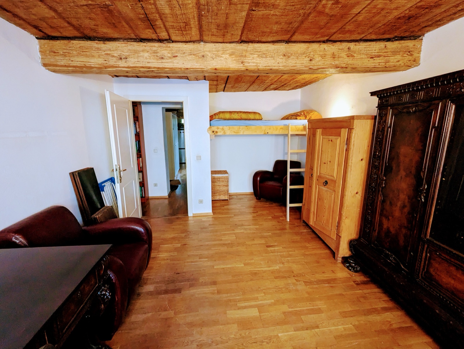 Wohnschlafzimmer mit Hochbett, Kleiderschrank, Ledersesseln und Holzbalkendecke, Blick zur Tür in den Vorraum
